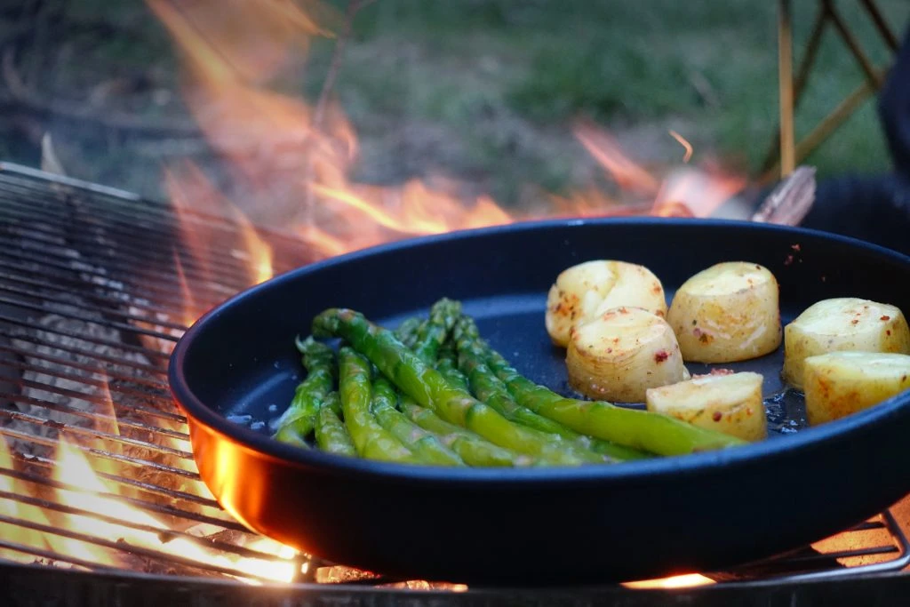 Asparagus and potatoes cooking in a pan over an open fire