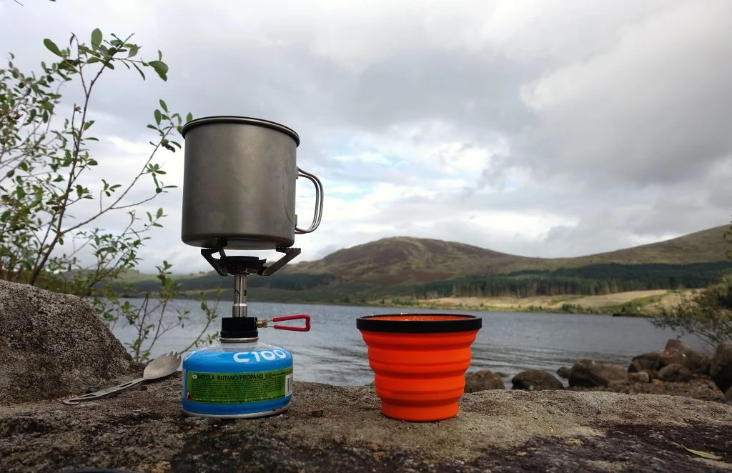 Stove and cup with a loch and hills in the background